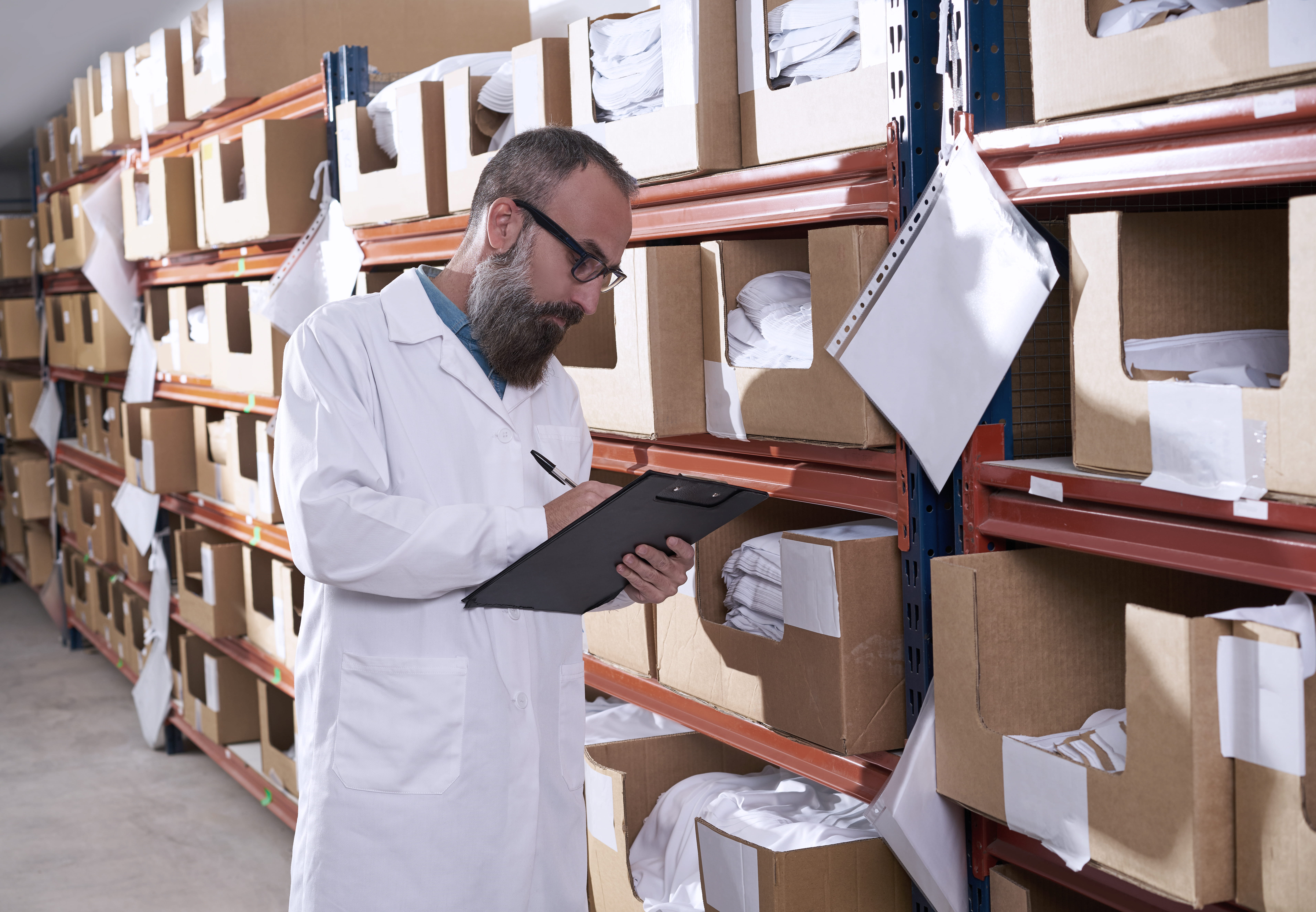 Medarbeider noterer i dokument mens han kontrollerer lagerreoler